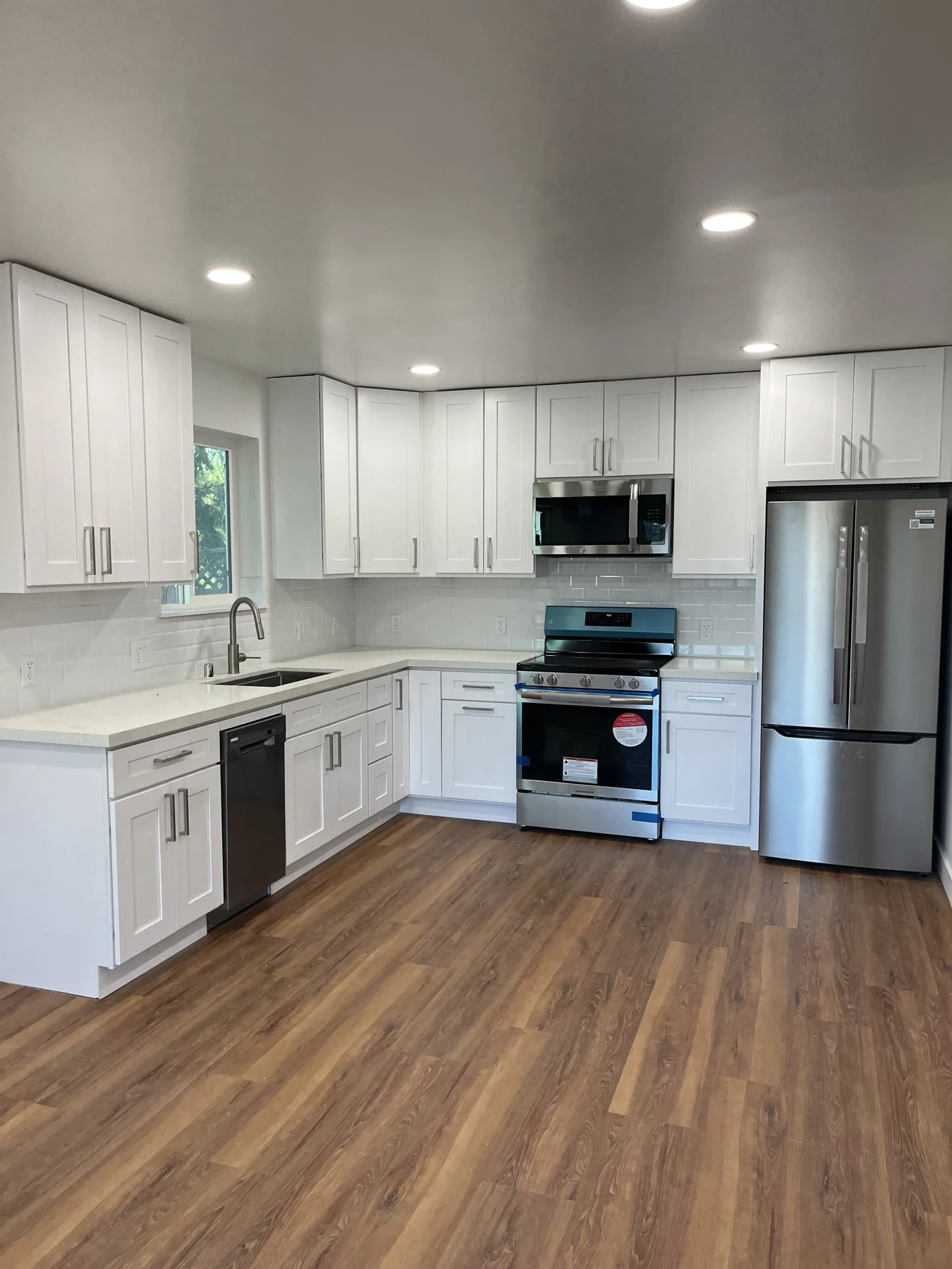 ADU kitchen with white cabinets, stainless appliances and wood-look flooring.