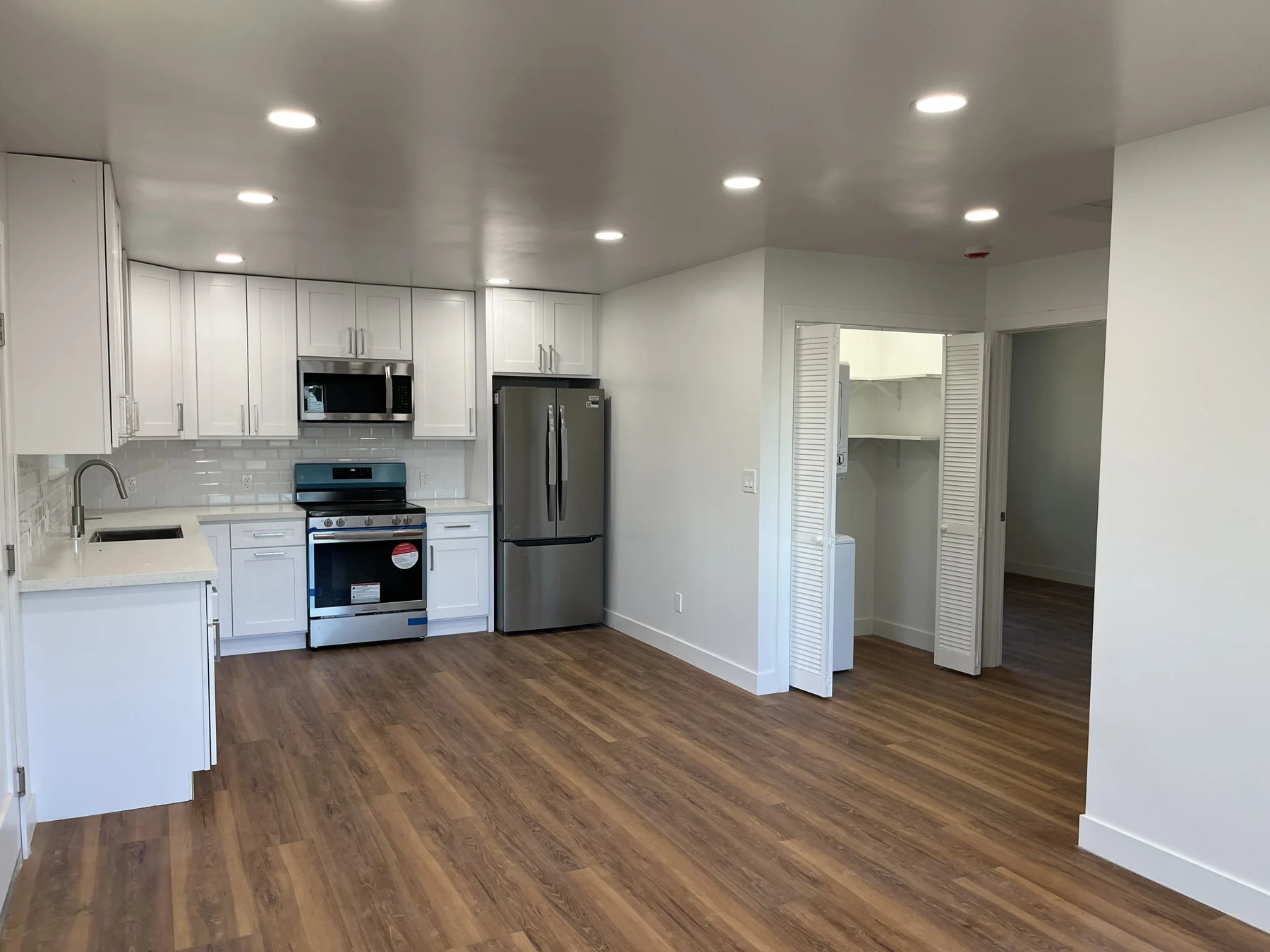 ADU kitchen and living area with white cabinets and wood-look flooring.