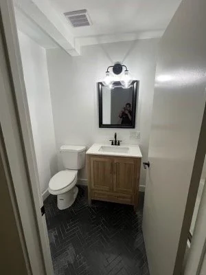 Compact bathroom with a wood vanity, white toilet and wall mirror.