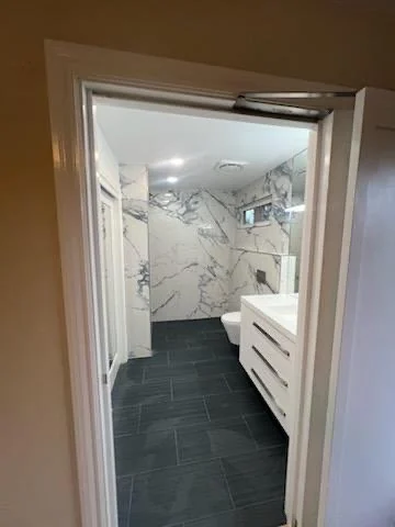 Bathroom viewed through a doorway with marble-pattern wall tile and dark floor.