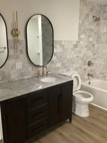 Bathroom with a wood vanity, round mirror and pale patterned shower tile.