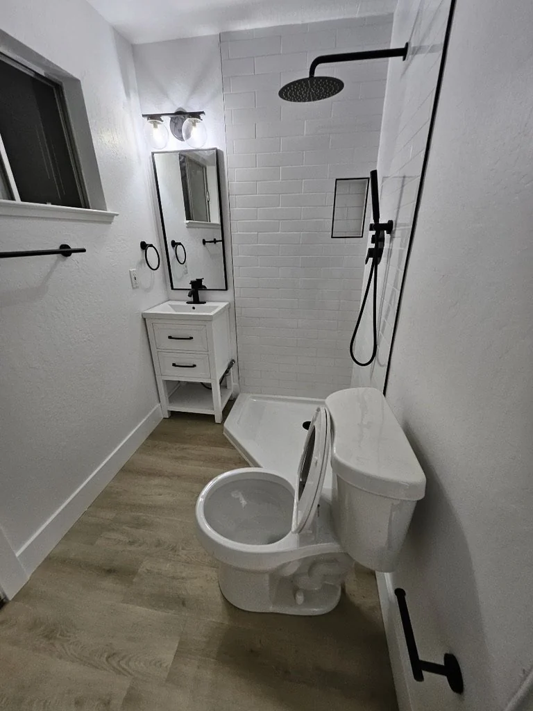 Bathroom with white tile, black shower fixtures and a compact basin.