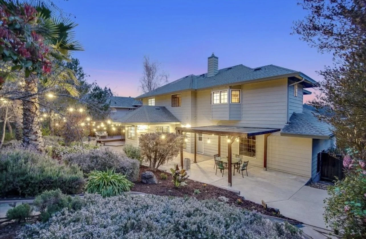 Painted house exterior with garden landscaping and an illuminated patio.