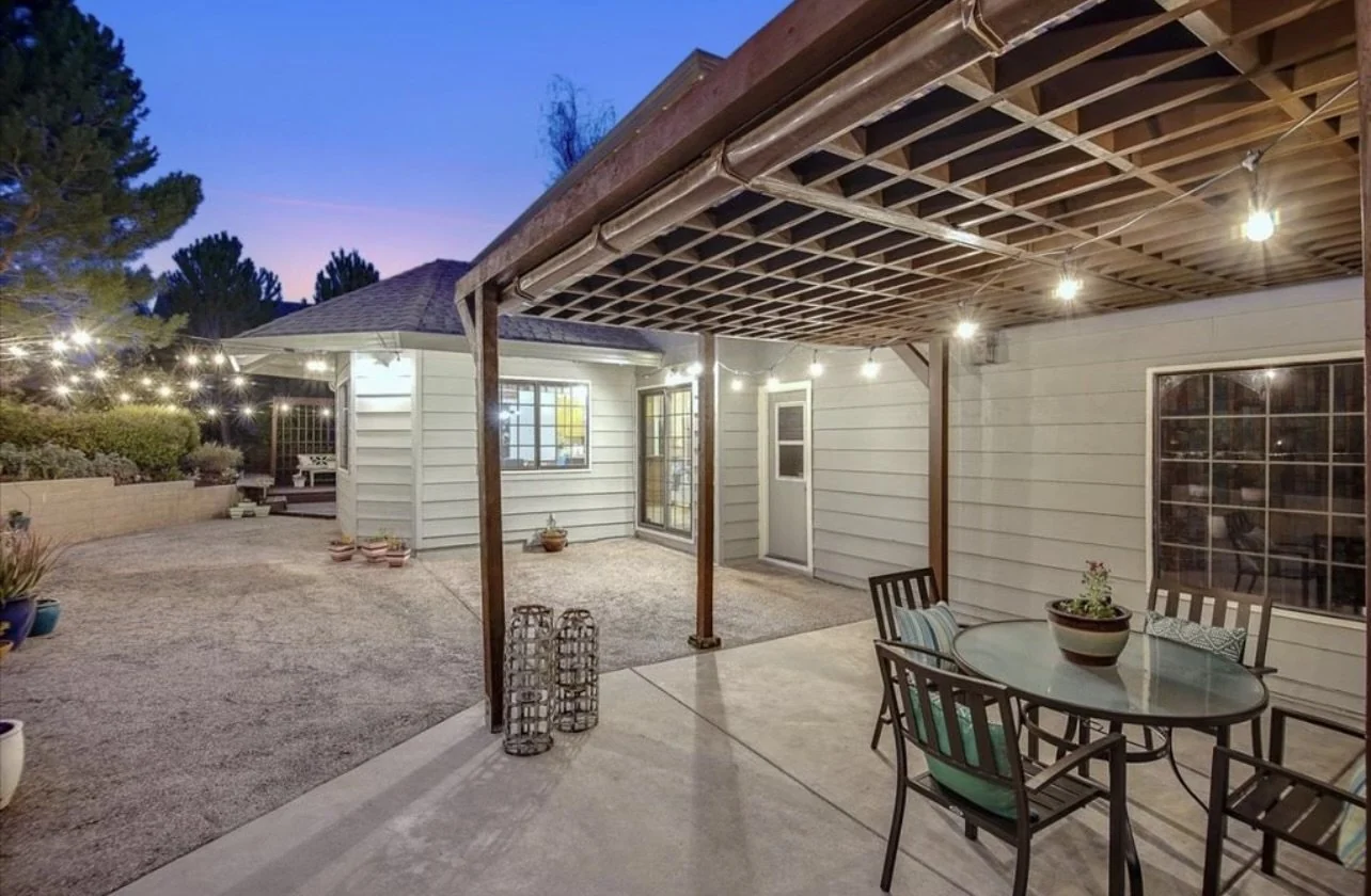 Covered patio with painted siding, exposed roof beams and outdoor seating.