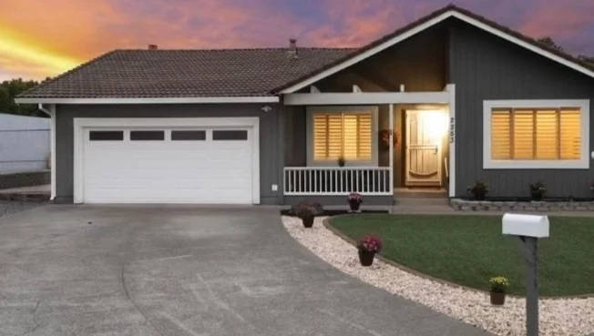 Single-story painted house with an illuminated porch and white garage door.