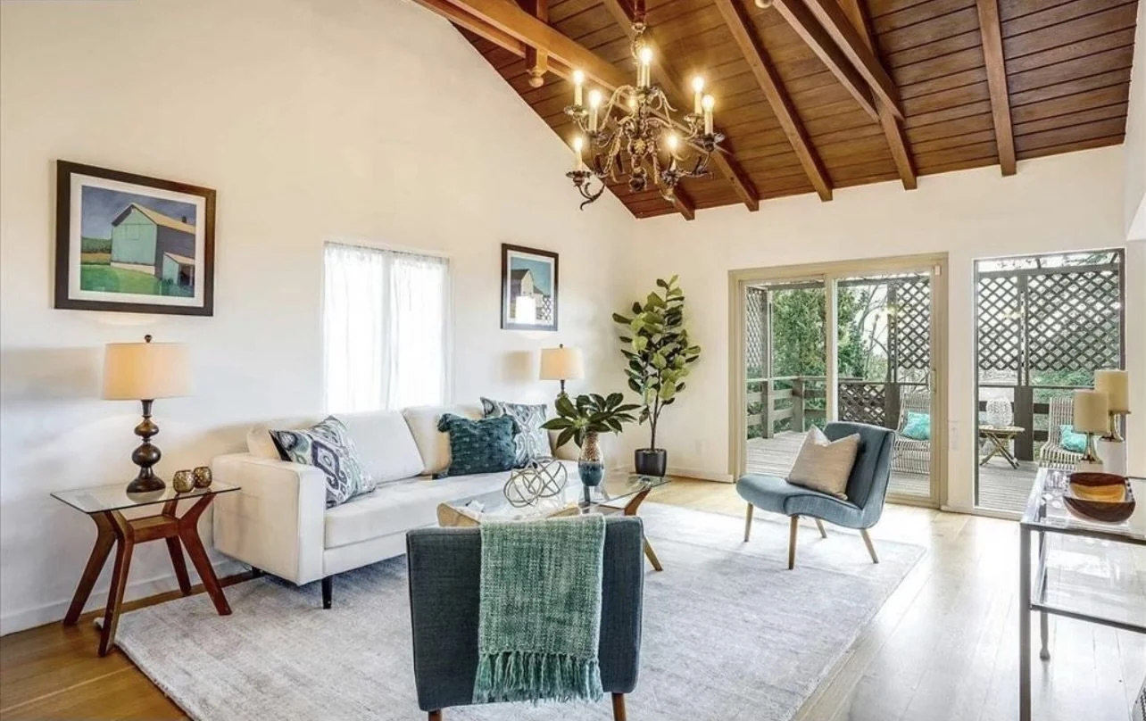 Living room with exposed wood beams, fresh white walls and green seating.