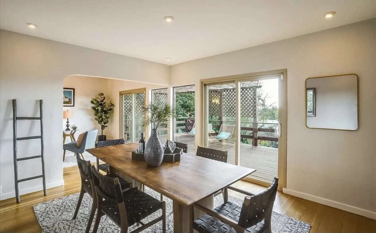 Dining room with pale walls, a dark table and large windows.