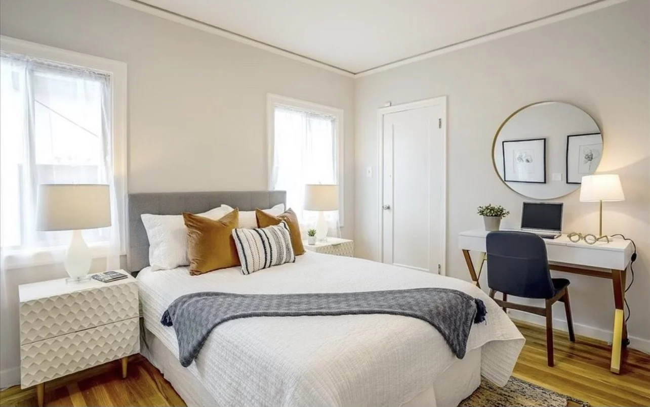 Bedroom with pale walls, a wood bed and windows on two sides.