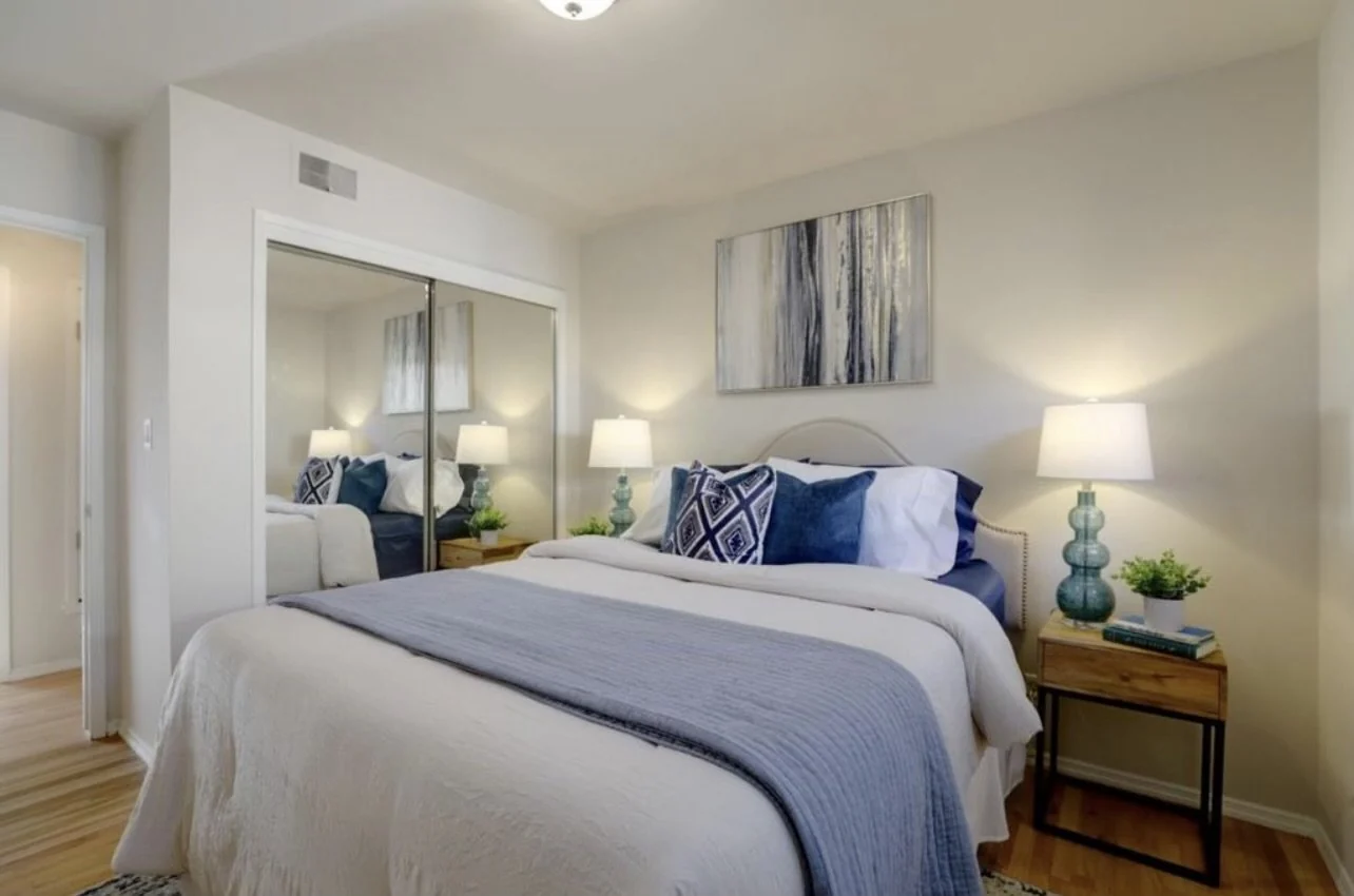 Bedroom with pale walls, blue bedding and white mirrored closet doors.