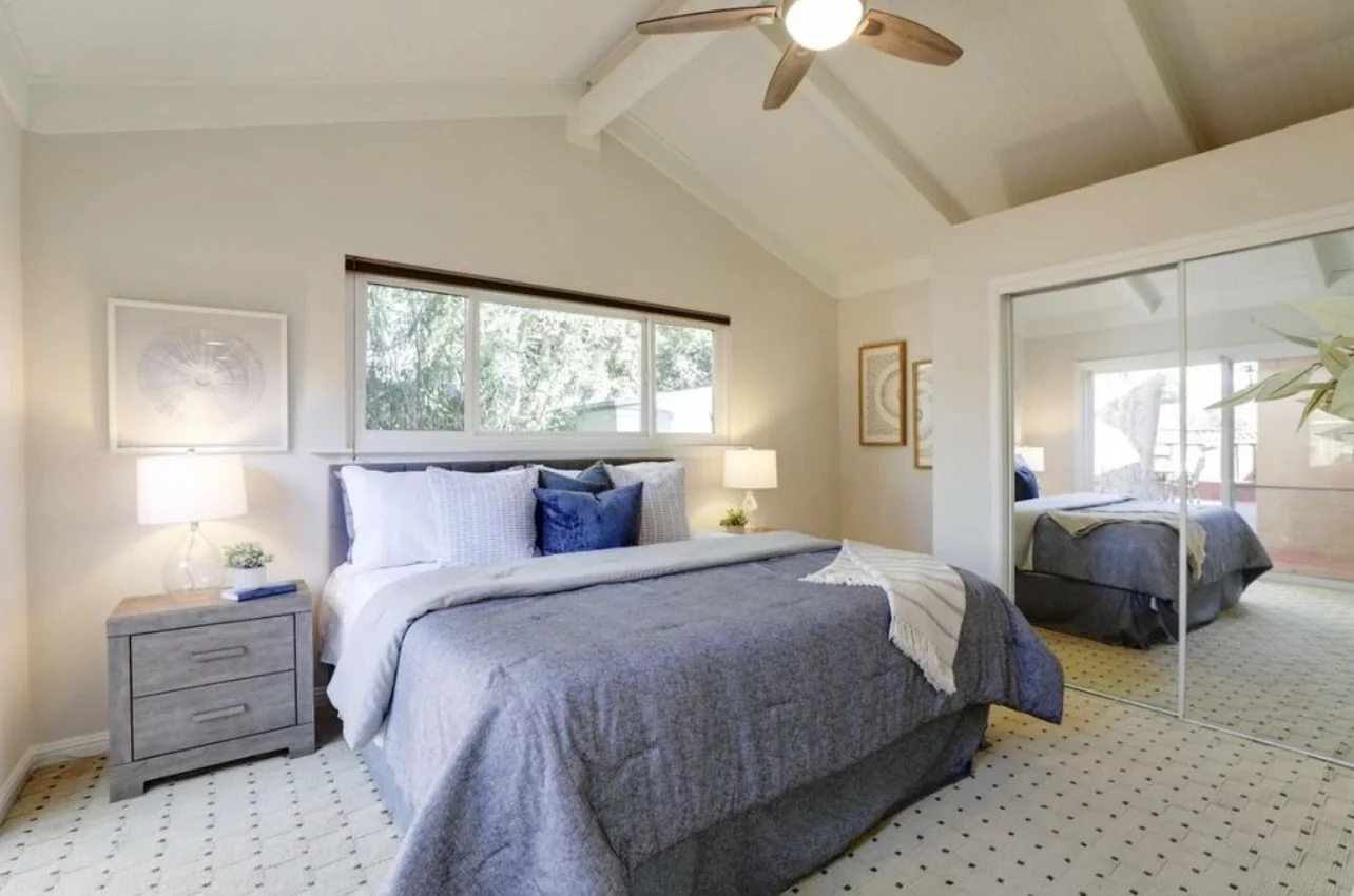 Bedroom with pale walls, a ceiling fan and a seating area.