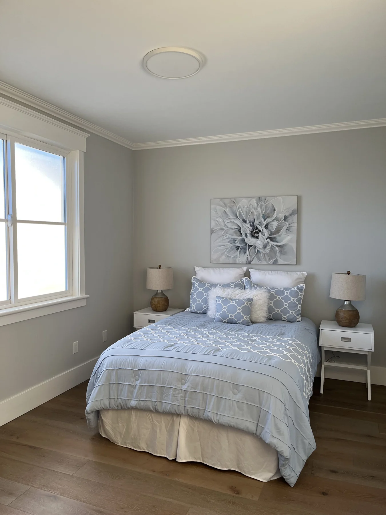 Bedroom with freshly painted pale walls, wood flooring and a white bed.