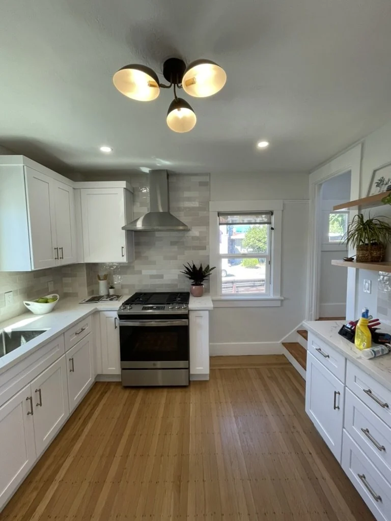 White kitchen with wood floors, gray backsplash and a statement ceiling light.