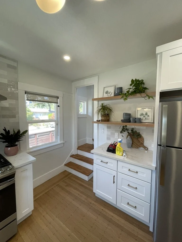 White kitchen with open shelves, gray backsplash and wood flooring.