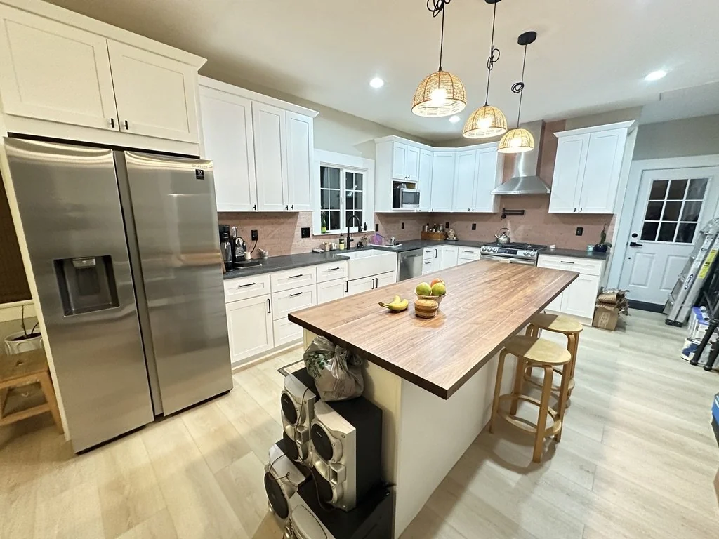 White kitchen with a stainless refrigerator, wood island and pendant lights.