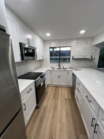 Galley kitchen with white cabinetry, gray backsplash and wood flooring.